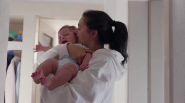 Anne ağlayan bebeğini kucağında tutuyor, bebeğin yanağına bir öpücük bastırıyor bebek çırpınıyor ve dışa doğru uzanıyor. Çiğ ve filtresiz annelik anı..