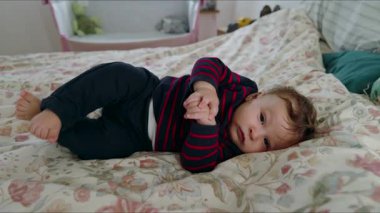 Bebek yatakta uzanıyor, baş parmağını gevşek bir ifadeyle emiyor, sakin ve huzurlu bir an, çocuk sıcak aile yatak odasında dinleniyor ve pencerelerden içeri ışık giriyor.