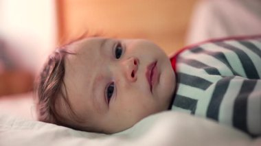 Uykulu bebek yatakta uzanıyor, rahat bir ifadeyle yavaşça bakıyor, rahat bir ev ortamında huzur içinde dinleniyor.