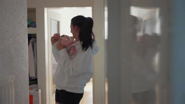 Anne, bebeğini koridorda göğsüne yakın bir yere yatırıp yüzünü çocuğa bastırıyor. Aynaya yansıyan anın yansıması.