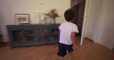 Çocuk hızla bir koridorda köşeyi dönüyor, hız ve heyecanla koşuyor, ev ortamında hızlı hareket ve hareket gösteriyor, enerjik ve oyuncu hareketler sergiliyor