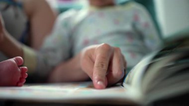 Annenin bir bebeği tutarken bir kitabı işaret ettiği ve büyük çocuğuyla koltukta oturduğu, hikaye anlatıcılığıyla dolu bir aile bağı kurduğu yakın plan..