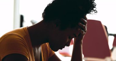 Genç Afrikalı Amerikalı kadın evde depresyonla boğuşuyor. Stres ve keder altında eziliyor. Baş ağrısı çeken elleri şakaklara koyuyor.