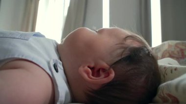 Yatakta uzanan bebek, yandan gören, yumuşak saçlı ve hafifçe gülümseyen.