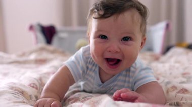 Yatakta uzanan bebek, neşeli kahkahalar, geniş bir ağız, neşeli ve mutlu bir an, erken çocukluk hazzı, sıcaklık ve ev ortamında rahatlık.