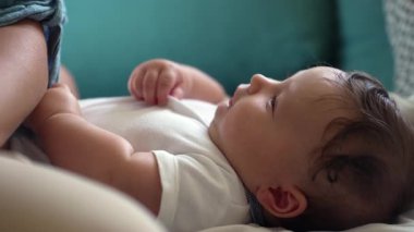 Bebek yumuşak yüzeyde yatıyor, neşeli bir ifadeyle gülümsüyor, rahat duruş, huzurlu bir an, erken çocukluk gelişimi, rahat bir ev ortamı, bakım