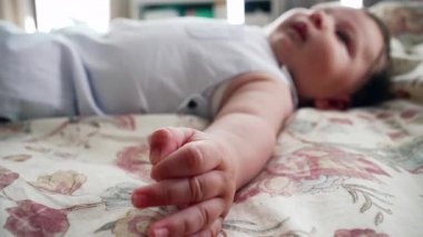 Bebek rahat bir şekilde battaniyeye uzanmış, tek kolla uzanıyor. Sahne, bebekleri rahat bir evde dinlenirken tüm vücudunu yakalar.