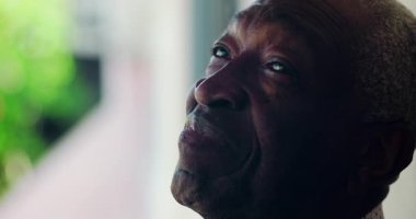 Afro-Amerikalı yaşlı bir adam, sakin ve yansıtıcı bir tavırla yukarıya bakıyor, duvara yaslanıyor, duygusal derinlik ve bilgelik gösteriyor.