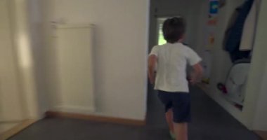 Çocuk enerjik bir şekilde koridorda bir odaya doğru koşuyor, çocuk evin içinde hareket ederken, içeride heyecan ve aktif enerji gösteriyor..