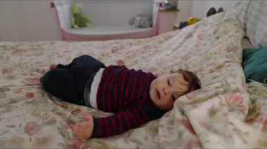 Bebek yatakta uzanıyor, kollarını açmış, ilgi ve rahatlık arıyor, sıcak aile yatak odasında, yumuşak bir yatak ve doğal ışık ile telaşın erken belirtileri.