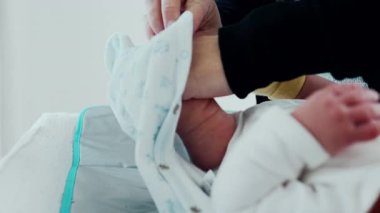 Ebeveyn bebeği yatakta nazikçe giydirirken bebek yukarı bakar, kollar yukarı, doğal duygularla dolu samimi bir ev ortamı, bakım, rahatlık ve bağlanma anlarına odaklanır.