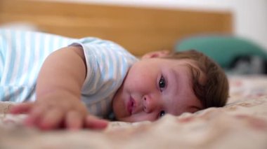 Bebek yatakta uzanıyor, elini uzatıyor, çevreyi keşfediyor, çocukluk merakı, sıcak ve rahat ev ortamı.