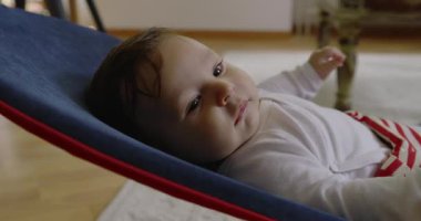 Bebek bir fedaide yatıyor, gülümsüyor ve mutlu görünüyor, rahat bir ev ortamında bir anlık mutluluğun ve konforun tadını çıkarıyor, erken çocukluğun neşesini ve masumiyetini vurguluyor.