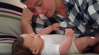 Anne kanepeye uzanıp bebeğine bakıyor. O da kanepede yatıyor. Huzurlu bir bağ ve sakin bir bağ anı.