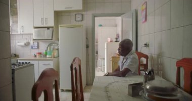 Bir yaşlı siyah adam mutfak masasında oturmuş, kollarını dinlendiriyordu. Etrafı fayanslarla, duvarlarla, buzdolabıyla ve rahat bir ev ortamında ahşap sandalyelerle çevriliydi.