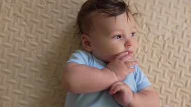 Bebek paspasın üzerinde uzanıyor, elini emiyor, kendini yatıştıran davranış, erken gelişim, refleks, rahatlama ifadesi, güvenli, huzur verici bir ortamda huzurlu bir an.