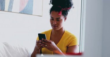 Genç Afrikalı Amerikalı kadın evdeki kanepeye mesaj atıyor. 20 'li yaşlarda Latin kökenli samimi bir kız arkadaşlarıyla internet üzerinden iletişim kurmak için modern teknolojiyi kullanıyor.