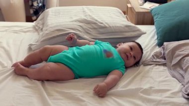 Yatakta uzanan bebek, meraklı bebek çevreyi gözlemliyor, rahat duruş, erken çocukluk keşfi, nazik hareketler, rahat ev ortamında huzurlu bir an.
