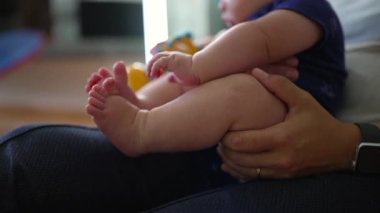 Annenin kollarında dinlenen bebek, bacaklar hafifçe bükülmüş, gevşemiş ve güvenli, şefkatli kucaklama, erken çocukluk rahatlığı, nazik bakım, sıcak ve sevgi dolu aile bağı