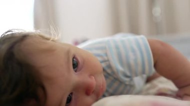 Yatakta uzanan bebek, yakından bakma, yumuşak ve meraklı ifade, nazik çocukluk anı, sıcak ve huzurlu ev atmosferi, erken duyusal keşif