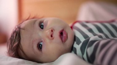 Bebek yatakta uzanıyor, masum bir ifadeyle başını kaldırıyor, rahat bir yuva ortamında merakla ve sessizce dünyayı keşfediyor.