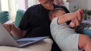 Anne dizüstü bilgisayarda çalışırken bebek elini tutuyor, uzaktan işleri ve çocuk bakımını dengeliyor, modern ebeveynlik, çoklu görev, ev işi, sorumluluk, kariyer, aşk.