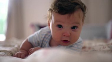 Yatakta uzanan bebek, neşeli yüz ifadesi, neşeli merak, keşif çevresi, sıcak ve rahat an, erken çocukluk duyusal keşif, rahat yuva kurma