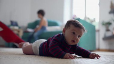 Bebek karnının üstünde yatıyor, kollarının üzerinde dinleniyor, derin düşüncelere dalmış bir ifadeyle ileri bakıyor, erken gelişim, mide zamanı, çevreyi gözlemleme, kapalı alanda çocukluk anı.