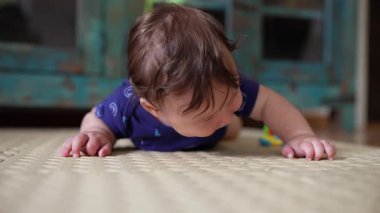 Bebek mindere uzanıyor, elleri öne doğru uzanmış yüz üstü yatıyor, erken hareket keşfi, duyusal deneyim, çevreyi keşfetme, bebek gelişimi anı