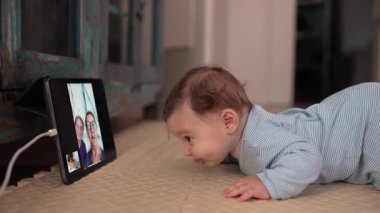 Bebek mindere uzanıp video çağrısı sırasında tablet izliyor, heyecandan ağzı sulanıyor, erken duyusal tepki, sanal aile etkileşimi, günlük hayatta teknoloji