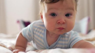 Bebek yatakta uzanıyor, odaklanmış bakışlarla uzanıyor, duyusal keşiflerle meşgul, sıcak ve rahat bir an, erken çocukluk keşfi ve merakı