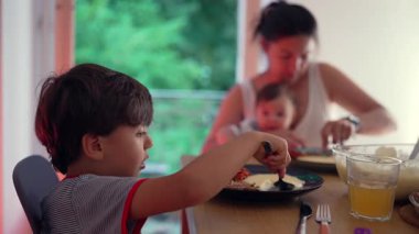 Aile sofrasında yemek yiyen küçük bir çocuk, büyük bir lokma, ev yemeği, aile birliği, günlük ebeveynlik, konforlu ev dekorasyonu, çocuğun yemekten keyif alması, günlük yemek saati..