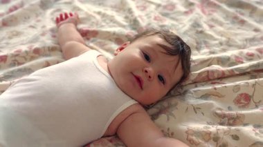 Yatakta uzanan bebek, neşeyle gülümseyen, gevşemiş an, sıcaklık, masumiyet, ebeveyn-çocuk bağı, erken gelişim, mutluluk, aile bağı, güvenlik, güven