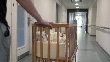 Yeni doğmuş bir bebekle el yordamıyla hastane koridorunda bebek beşiği itmek, yeni doğan bakımının ilk haftasını, aile, ebeveynlik ve sağlık hizmetleri için ideal olduğunu gösteriyor.