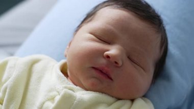 Yeni doğmuş bebek huzurlu bir ifadeyle uyuyor, mavi bir yastığın üzerinde dinleniyor. Hassas özellikler ve dingin atmosfer, masumiyet ve yeni doğan hayatın sükuneti.