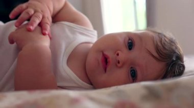 Yatakta uzanmış bebeğe yakın çekim, merakla bakmak, el uzatma, erken duyusal gelişme, bağlantı, çocukluk masumiyeti, huzurlu bir an, güven.