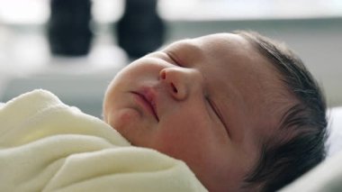 Yeni doğmuş bebek, yumuşak sarı bir battaniyeye sarılı huzurlu bir ifadeyle uyuyor. Yeni doğan hayatın masumiyetini ve sükunetini vurgulayan hassas özellikler.