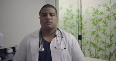 Steteskopla klinikte dikilen ciddi erkek doktor, modern tıp ortamında sakin bir otorite ve profesyonel hazırlık gösteriyor.