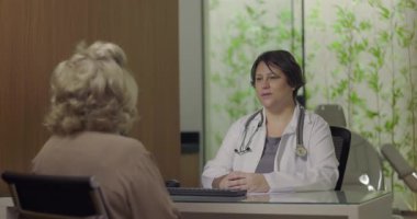 Steteskoplu doktor, klinikteki sağlık muayenesi sırasında yaşlı kadın hastayla konuşmaya odaklanmış.