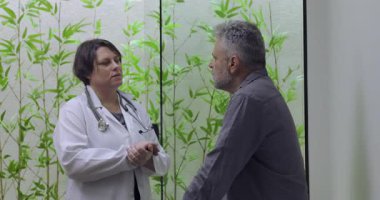 Kadın doktor, sağlık danışmanlığı sırasında orta yaşlı erkek hastayla iletişim kuruyor, profesyonel tıp ortamında rehberlik ve netlik sağlıyor.