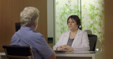 Doktor muayenehanede muayene sırasında erkek hastayı dinliyor. Profesyonel sağlık ortamında sakin tavır ve özenli vücut dili ile.