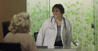 Steteskoplu gülümseyen doktor profesyonel klinikteki tıbbi danışmanlık sırasında yaşlı kadın hastayla samimi bir şekilde temas kuruyor.