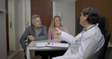 Doktor, klinikteki danışma sırasında orta yaşlı kadın hasta ve destekleyici erkek arkadaşla sağlık konularını tartışıyor.