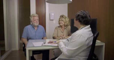 Kıdemli erkek ve kadın, muayenehanedeki ortak tıbbi danışma sırasında doktorla sağlık konularını tartışıyor.