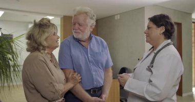 Yaşlı çift, iyi tıbbi haberleri aldıktan sonra, klinik koridorunda aşk ve kutlama için kadın doktorun önünde öpüşüyor.