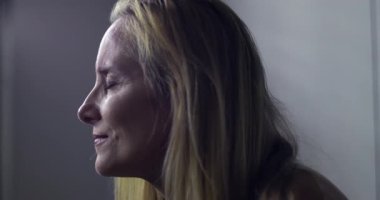 Klinikteki kadının yoğun, duygusal bir ifadeyle yan tarafa baktığı yakın plan. Arka planda serum var. Tıbbi tedavi ya da iyileşme öneriliyor.