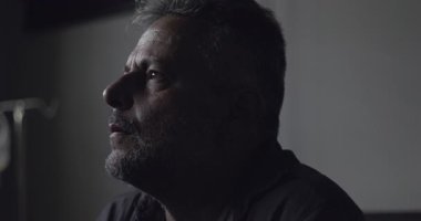 Karanlık klinikte eli yüzü kapalı sıkıntılı bir adamın yakın çekimi, tanıya karşı duygusal tepki ya da düşük ışıkta yakalanan iç kargaşa