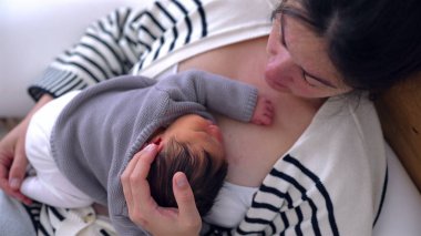 Annenin, uyuyan bebeğini göğsüne yaslayıp kucağında kucak açtığı ve sevgi ve şefkatle bebeğe baktığı yakın plan. Samimi bağ ve anneliğin koruyucu doğası.