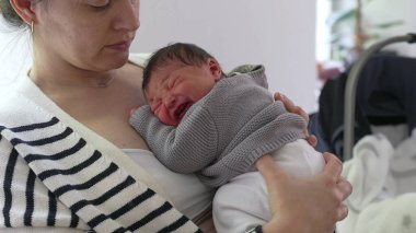 Anne, yeni doğmuş bebeğini göğsüne yakın bir yere yatırıyor, sıcaklık ve bakım yayıyor. Huzurlu bir ev ortamında anne ve çocuk arasındaki şefkat ve derin bağ