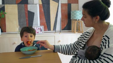 Kadın, bebeğini rahat bir evde emzirirken oğluna spagetti yediriyor ve aynı anda birden fazla çocuğa bakan bir annenin yoğun hayatını anlatıyor.